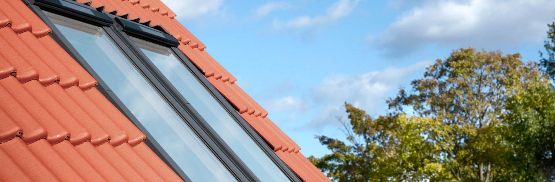 Twee gekoppelde VELUX dakramen in een rood pannendak met blauwe lucht en bomen