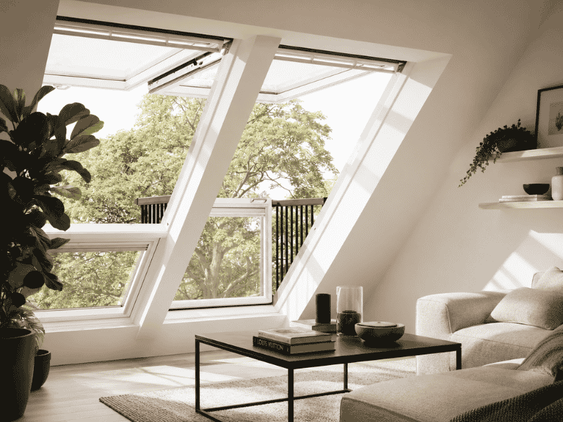 VELUX balkonvenster afmetingen in een moderne zolderkamer met geopend balkonvenster, veel daglicht en uitzicht op groene bomen.